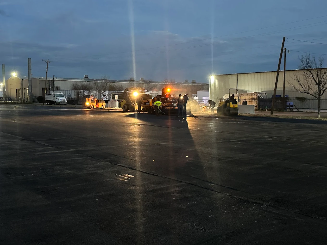 Night paving job under floodlights on a commercial lot